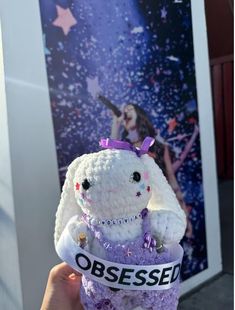 a person holding up a small stuffed animal in front of a wall with an advertisement on it