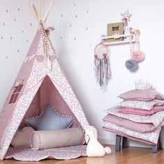 a pink teepee tent sitting on top of a wooden floor next to a pile of pillows