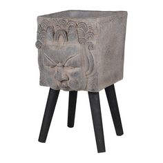 a small cement planter sitting on top of a black wooden stand with a face carved into it