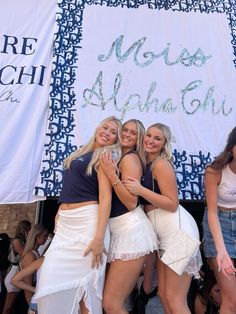 three beautiful young women hugging each other in front of a banner