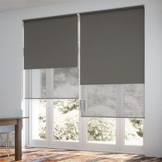 a living room with two windows covered in blinds and a wooden table next to it