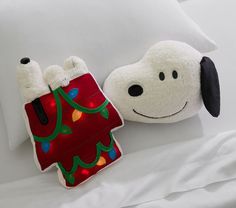 two stuffed animals laying on top of a white bed next to pillows with christmas lights