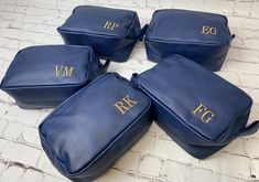 four blue leather bags with gold initials on the front and back, set against a brick wall