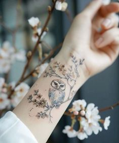 an owl tattoo on the wrist is shown in front of a branch with white flowers