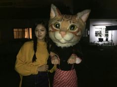 two women standing next to each other in front of a large cat mascot at night