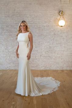 a woman standing in front of a brick wall wearing a white wedding dress with an open back