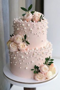 a three tiered cake with flowers and pearls on it's side, sitting on a table