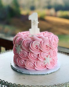 a pink cake with white frosting and a number one on top is sitting on a table