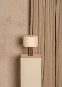 a lamp sitting on top of a white box next to a window with curtains behind it