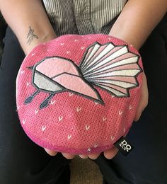 a person sitting on the ground holding a small pink bag with an image of a bird painted on it