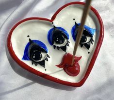 a heart shaped bowl with two birds painted on it and a wooden stick in the middle