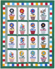 a quilted wall hanging with flowers in potted plants on it's sides