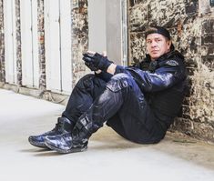 a man sitting on the ground in front of a brick wall with his feet up