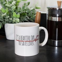 a white coffee mug sitting on top of a table next to a potted plant