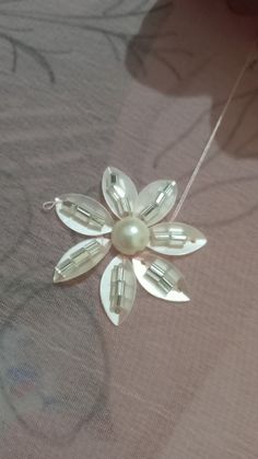 a white flower brooch with pearls on it's back end, sitting on a bed