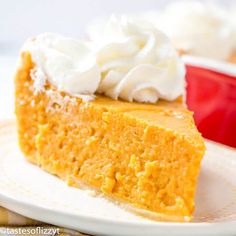 a slice of pumpkin cheesecake on a plate with whipped cream in the middle and a red bowl behind it