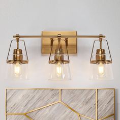 three light bathroom fixture with glass shades and gold accents on a white marble countertop