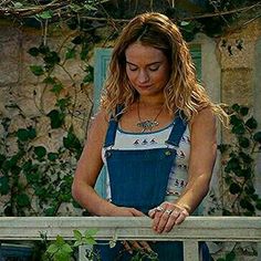 a woman in overalls standing next to a fence