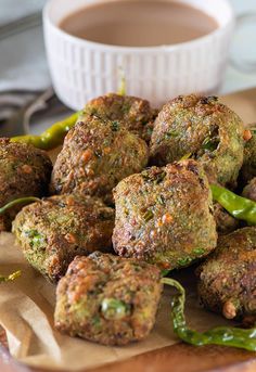 some meatballs are sitting on a table next to green peppers and a cup of coffee