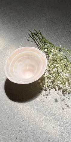 a white bowl sitting on top of a cement floor next to flowers and grass in the sun