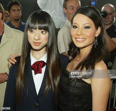 two young women standing next to each other in front of some people and taking pictures