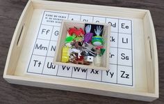 a wooden tray filled with different items on top of a wood table next to letters and numbers