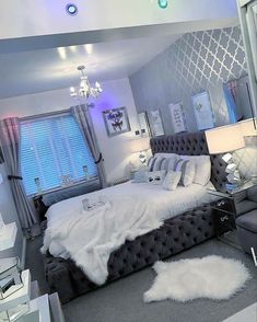 a bedroom decorated in white and grey with a large bed, chandelier, mirror windows, and lights on the ceiling