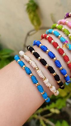 four different colored bracelets on someone's arm with green plants in the background