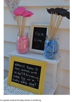 a table topped with jars filled with pink and blue candies next to a chalkboard sign