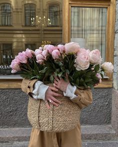 a woman holding a basket full of pink flowers in front of a storefront window