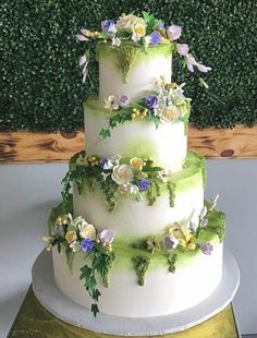 a three tiered wedding cake with flowers on top and greenery in the background