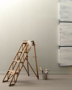 a ladder leaning against a wall next to a bucket and paintbrush on the floor