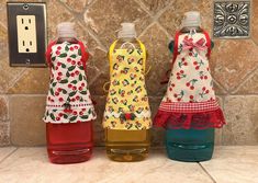 three bottles with aprons are lined up on the counter in front of a light switch