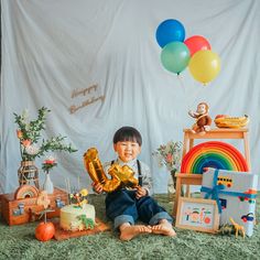 a little boy sitting on the floor with balloons and toys in front of him,