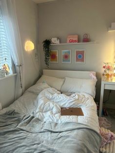 an unmade bed with white sheets and pillows in a bedroom next to a window