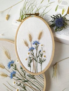 two embroidery hoops with blue and white flowers on them next to an open book