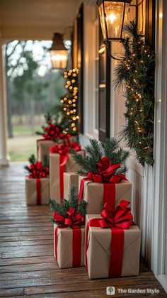 christmas presents are lined up on the front porch with red bows and lights hanging from them