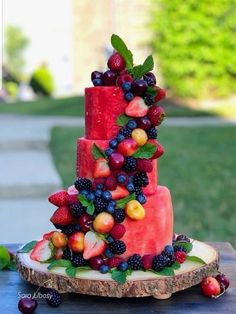 a three tiered cake with fruit on it sitting on top of a wooden slice