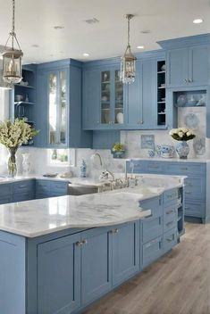 a kitchen with blue cabinets and marble counter tops in the center, along with two chandeliers hanging from the ceiling