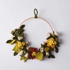 a wreath made out of felt with flowers and leaves hanging from the hoop on a white wall