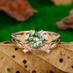 a close up of a ring on a leaf with green and white stones in the center