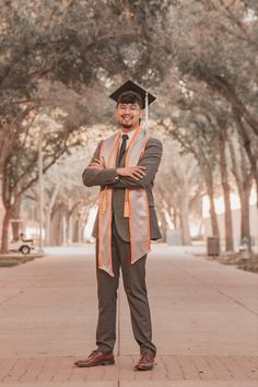 a man in a graduation cap and gown is standing on the sidewalk with his arms crossed