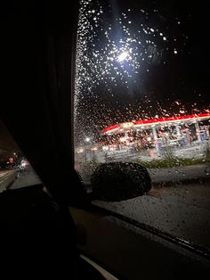 the view from inside a vehicle at night with rain on the windshield and street lights in the background