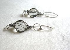 two silver wire wrapped earrings on a white cloth covered tablecloth, one is dangling from the end of each ear