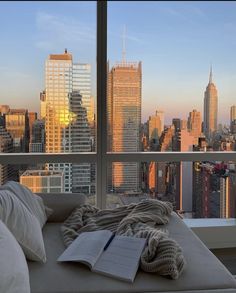 an open book is sitting on a couch in front of a window overlooking the city