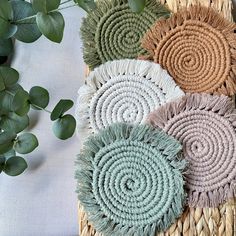 four woven coasters with different colors and sizes on a table next to some green leaves