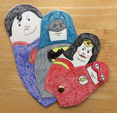 three children's handmade paper cut outs on a wooden surface with the image of superman and wonder woman