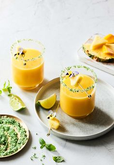 two glasses filled with orange juice and garnished with limes on a plate