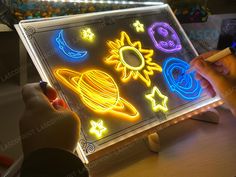 a child is drawing on a light box with neon lights and stars around it,