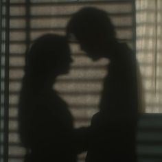 two people standing next to each other in front of a window with blinds on it